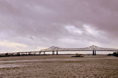 Suspension bridge over river against cloudy sky