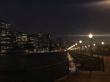 Illuminated buildings by street against sky at night