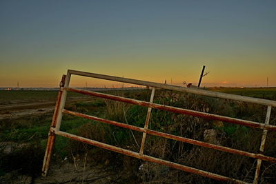 Fence on field against clear sky during sunset