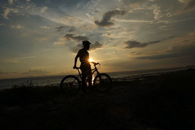 Silhouette man riding bicycle on sea during sunset