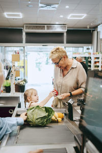 Granddaughter with grandmother standing near checkout at supermarket