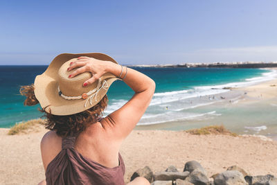 Rear view of woman wearing hat at beach against sky