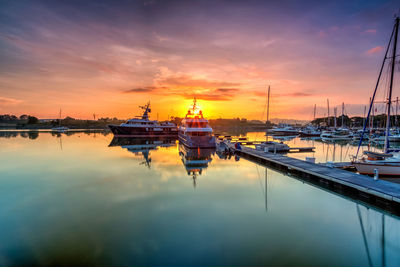 Sailboats moored at harbor against sky during sunset