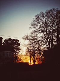 Silhouette bare tree and buildings against sky at dusk