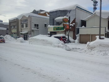 Snow covered houses by buildings in city