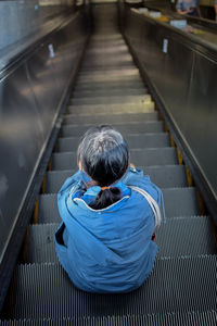 Rear view of woman sitting on escalator