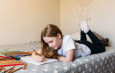 The girl after school plays at home, draws with pencils and felt-tip pens