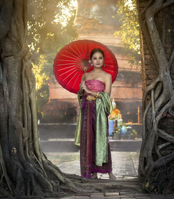 Portrait of young woman standing against tree