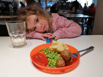 Portrait of cute girl leaning by meal on table at restaurant