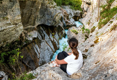 Rear view of young woman sitting on cliff above river gorge.