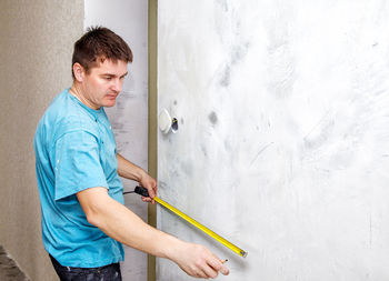 Side view of carpenter measuring wall at incomplete home