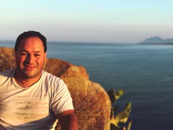 Portrait of man by retaining wall by sea against sky