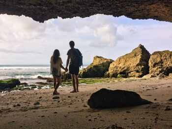 Rear view of couple holding hands while standing at beach