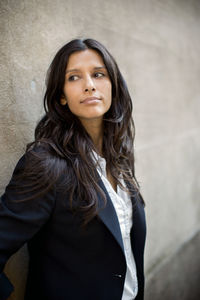 Woman looking away while standing against wall