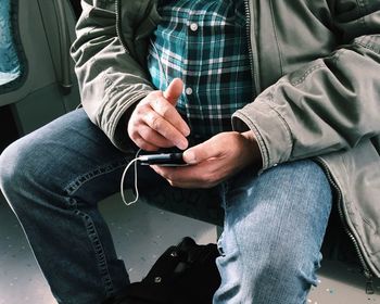 Midsection of man using mobile phone in train