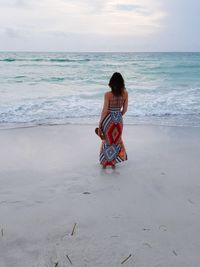 Rear view of woman standing on shore against sea at beach