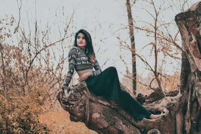 Portrait of young woman sitting on bare tree