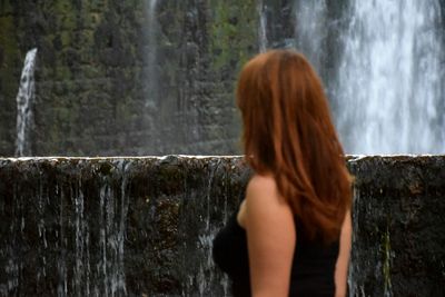 Rear view of woman standing against waterfall