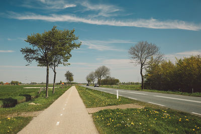 Empty road by field against cloudy sky