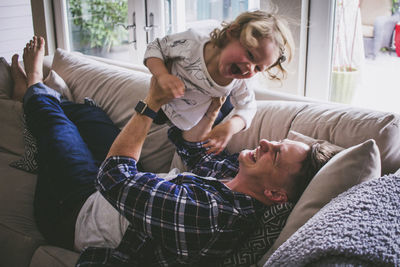 Happy father lifting up daughter while lying on sofa at home