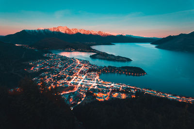 High angle view of illuminated city by sea against sky