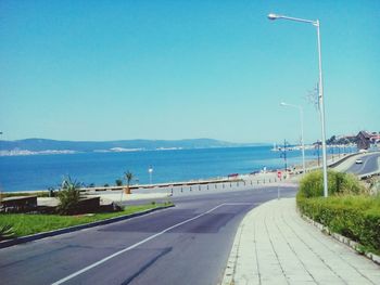 Road by sea against clear blue sky