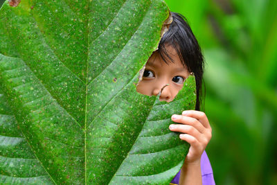 Close-up of girl hiding her face behind leaf