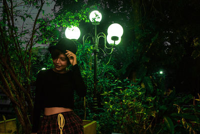 Young woman standing against illuminated plants at night