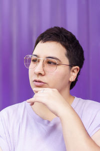 Thoughtful non-binary person with eyeglasses in front of purple corrugated wall