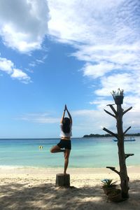 Woman doing yoga at beach against sky