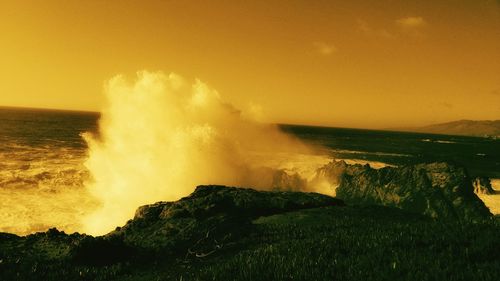 Sea waves splashing on rocks against sky during sunset