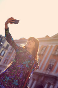 Woman photographing with mobile phone against sky