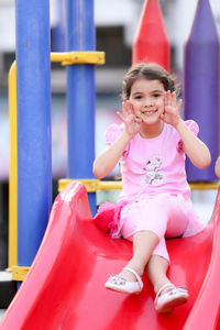 Portrait of girl gesturing while sitting on slide at park