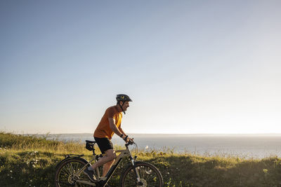 Mature sportsman riding electric bicycle by green plants