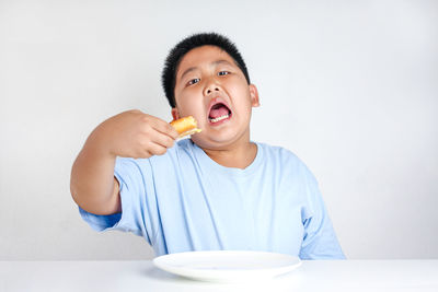 Portrait of boy eating food against white background