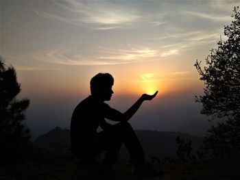 Optical illusion of silhouette man holding sun against sky