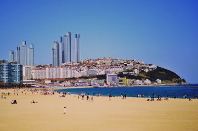 People on beach against clear blue sky