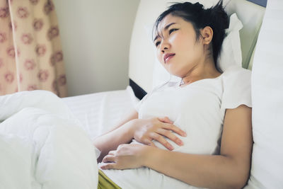 Young woman with hand on stomach in pain lying on bed at home