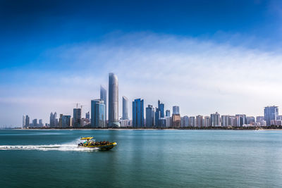 Sea by modern buildings in city against sky