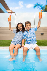 Two kids drinking orange juice in the swimming pool