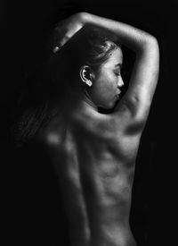 Rear view of topless woman against black background