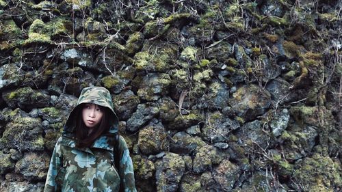 Woman in camouflage clothing standing against moss covered rocks