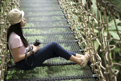 Side view of young woman sitting on metal structure