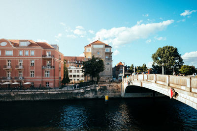 Bridge over river by buildings in city against sky