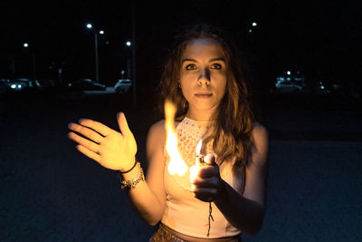 Portrait of young woman standing against illuminated lights at night