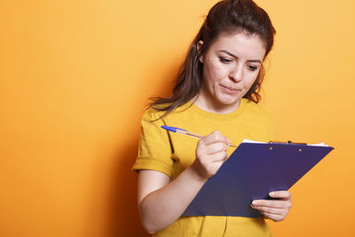 Young woman using digital tablet against yellow background