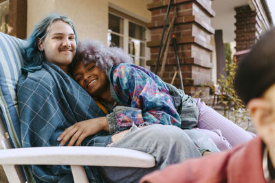 Portrait of smiling transwoman leaning on gay friend sitting on chair