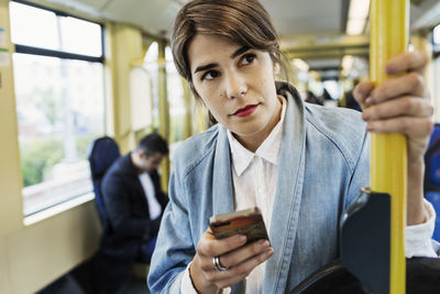 Thoughtful young woman using mobile phone in tram