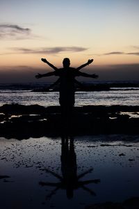 Silhouette man standing on beach against sky during sunset