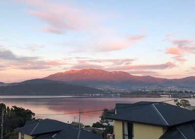 Houses by lake against sky during sunset